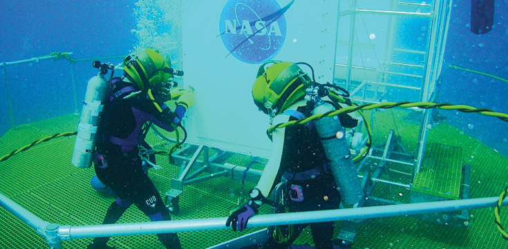Two people with diving gear underwater on a corrosion-resistant composite grating.